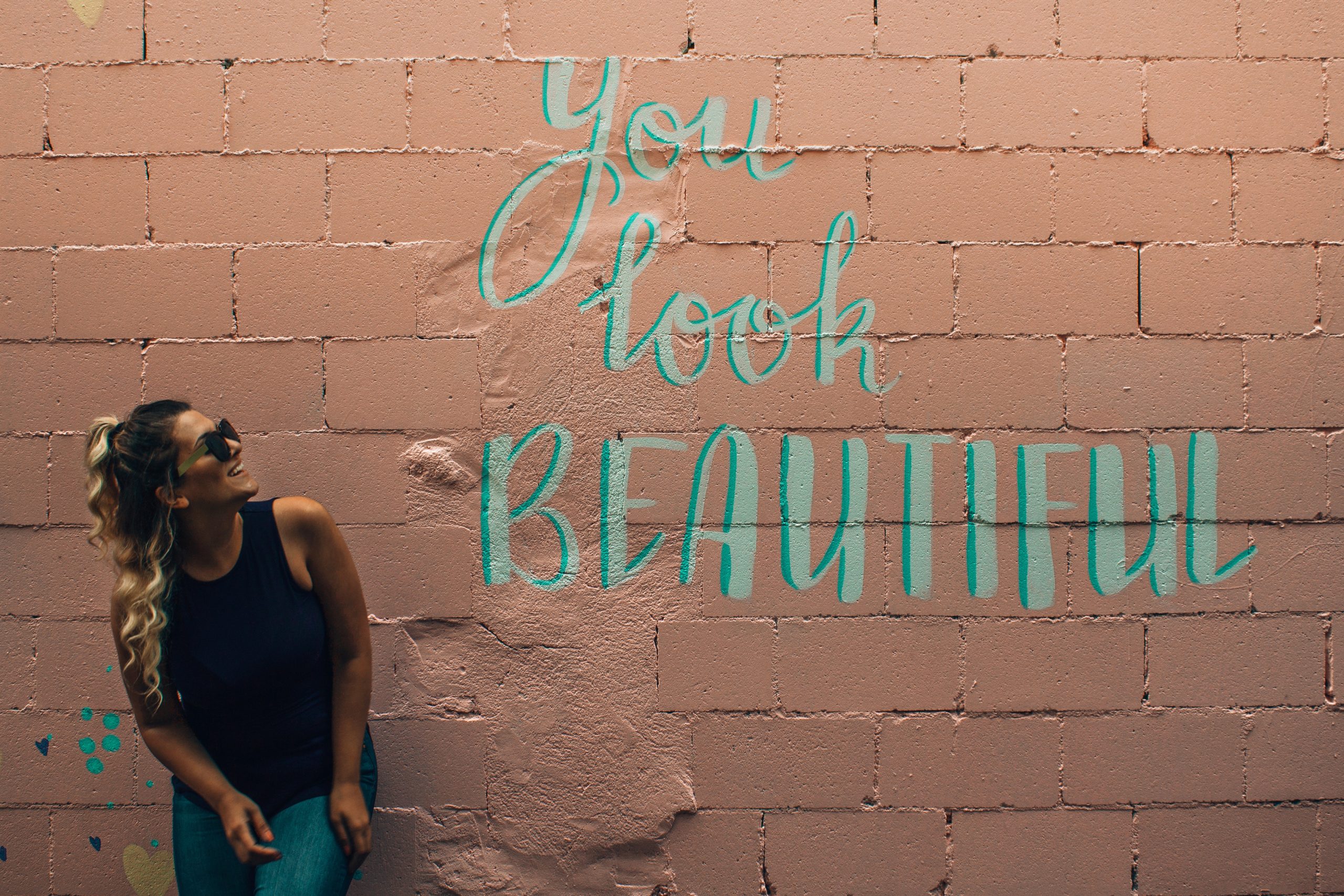 woman standing in front of a brick wall that says you look beautiful